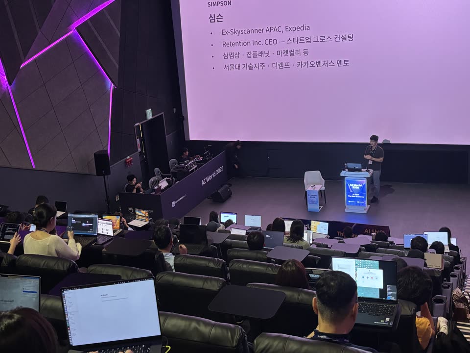 AI WORLD 2026 무대에서 심규섭이 발표하는 모습. 객석의 참가자들이 노트북으로 실습하고 있다.